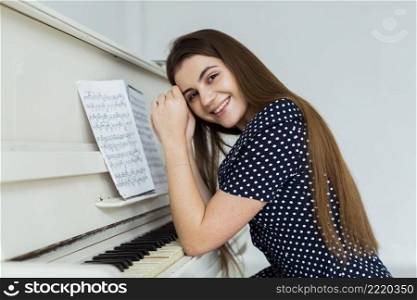 portrait smiling young woman leaning piano looking camera