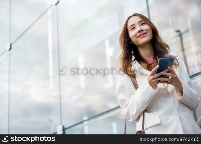 Portrait successful business woman smiling holding smartphone use application chat online in morning, Asian businesswoman working with mobile phone standing against street front building near office