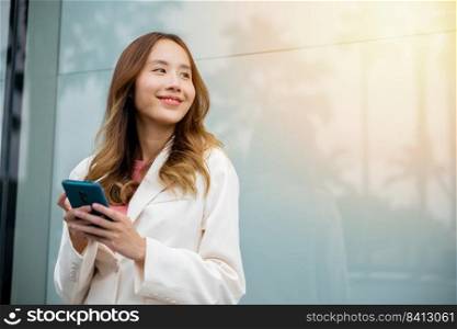 Portrait successful business woman smiling holding smartphone using app chat online in morning, Asian businesswoman typing text on mobile phone standing outdoors street front building near office