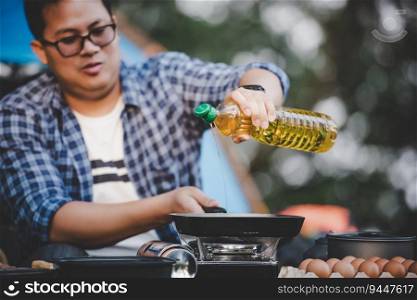 Portrait Thai traveler man glasses pouring sunflower oil into a frying pan. Outdoor cooking, traveling, camping, lifestyle concept.