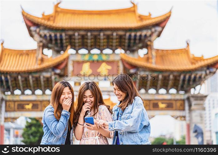 Portrait Three asian happiness women laughing and using smart mobile phone for social network together when travelling over the Jinbi square, Kunming, China, travel and tourism with friendship concept