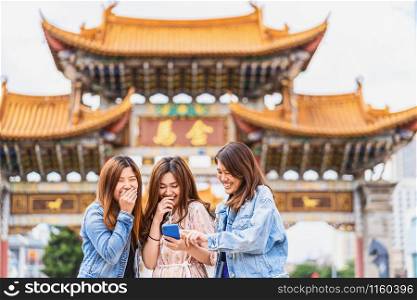 Portrait Three asian happiness women laughing and using smart mobile phone for social network together when travelling over the Jinbi square, Kunming, China, travel and tourism with friendship concept