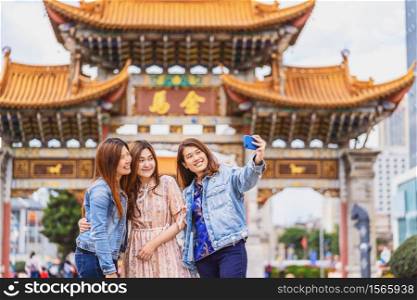 Portrait Three asian happiness women using smart mobile phone for selfie together when travelling over the Jinbi square, Kunming, China, travel and tourism with friendship concept