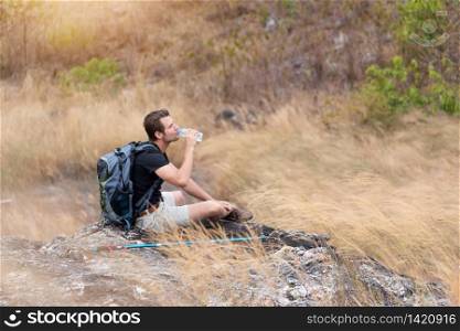Portrait Tired man traveler in black shirt drinking water. Male backpacker sitting relaxing on top of mountain in beautiful trail in countryside. copy space.