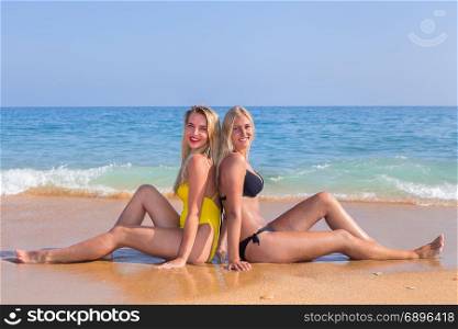 Portrait two young women sitting as friends on beach