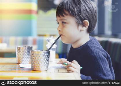 Portrait uhhappy kid drinking cold drink in restaurant,Toodler with funny face drinking soft drink with straw while waiting for food, Child with bored face sitting on couch and holding green creyon