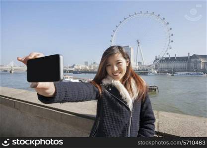 Portrait woman taking self portrait through cell phone against London Eye at London; England; UK
