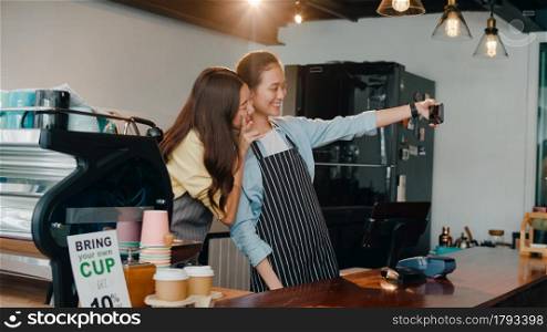Portrait young Asia female barista feeling happy with friend at urban cafe. Small business owner Korean girl in apron taking selfies on mobile phone looking to camera stand at counter in coffee shop.