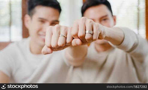 Portrait Young Asia Gay couple feeling happy showing ring at home. Asia LGBTQ+ men relax toothy smile looking to camera while hug in modern living room at house in the morning concept. Close up Shot.