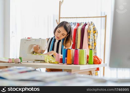 Portrait Young Asian designer woman working by sewing with sew machine at workplace, small business startup, Business owner entrepreneur, modern freelance job lifestyle concept.asean people