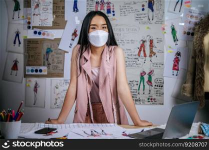 Portrait young asian female standing in modern atelier. Positive woman creative worker wearing medical face mask in studio. distance and new normal concept 