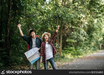 Portrait Young asian handsome man with backpack and trekking hat and pretty girlfriend standing and checking direction on paper map while walking on forest trail, backpack travel concept 