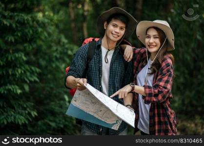 Portrait Young asian handsome man with backpack and trekking hat and pretty girlfriend standing and checking direction on paper map while walking on forest trail, backpack travel concept 