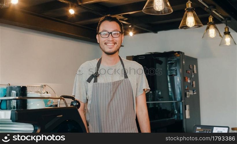 Portrait young Asian man barista feeling happy smiling at urban cafe. Small business owner Japanese male in apron relax toothy smile looking to camera standing at the counter in coffee shop.