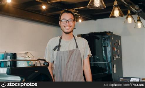 Portrait young Asian man barista feeling happy smiling at urban cafe. Small business owner Japanese male in apron relax toothy smile looking to camera standing at the counter in coffee shop.