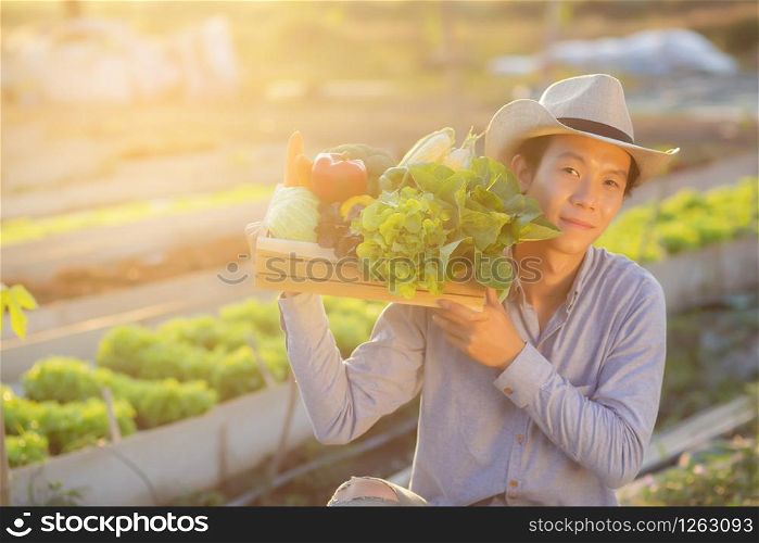 Portrait young asian man smiling harvest and picking up fresh organic vegetable garden in basket in the hydroponic farm, agriculture and cultivation for healthy food and business concept.