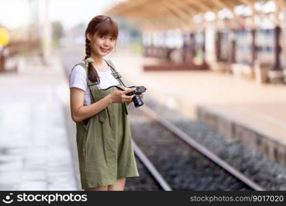 Portrait Young asian woman smiling tourist Traveler girl walking and with a holding the camera waits train travel journey is taken in railway platform Thailand, summer relax vacation Concept.