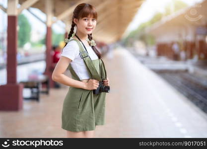 Portrait Young asian woman smiling tourist Traveler girl walking and with a holding the camera waits train travel journey is taken in railway platform Thailand, summer relax vacation Concept.