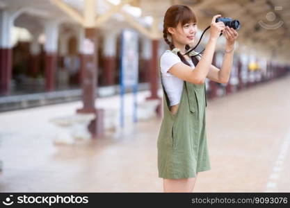 Portrait Young asian woman smiling tourist Traveler girl walking and with a holding the camera waits train travel journey is taken in railway platform Thailand, summer relax vacation Concept.