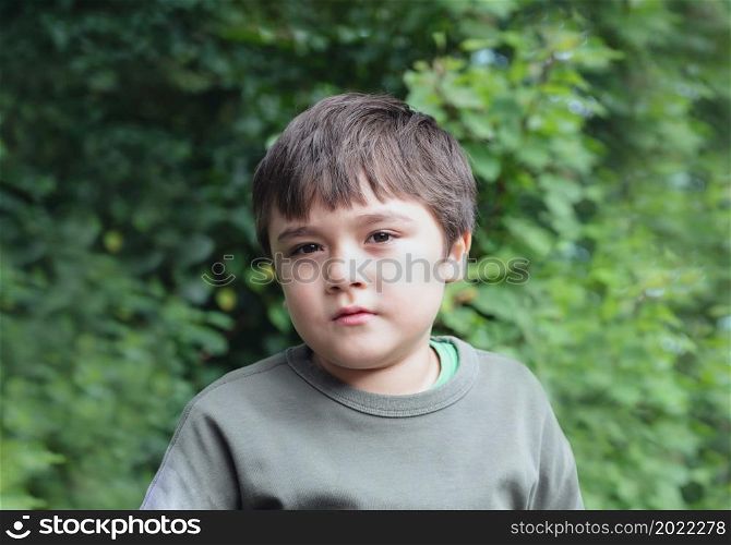 Portrait Young boy looking out deep in thought, School kid sitting alone on in the garden, Cute Child playing outdoor with blurry green nature in the park