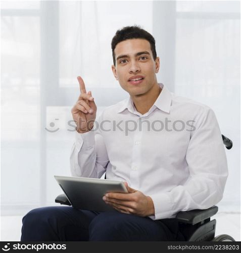 portrait young businessman sitting wheelchair holding digital tablet hand pointing his finger upward