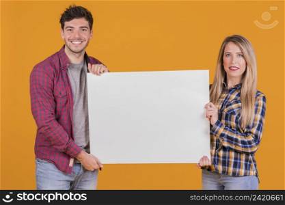 portrait young couple presenting white placard against orange backdrop