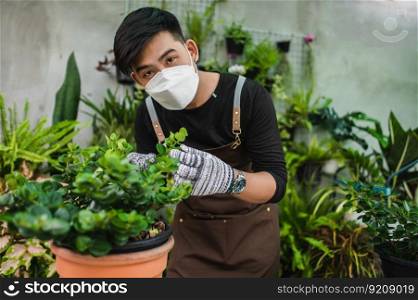 Portrait young gardener man wearing face mask and apron with gloves take care a houseplants in hand looking to camera