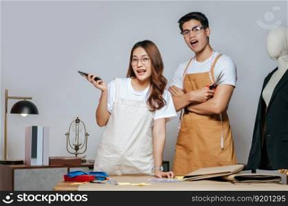 Portrait Young handsome man and pretty woman, Couple fashion designer working with smartphone, paper clothing pattern on desk at the studio at home