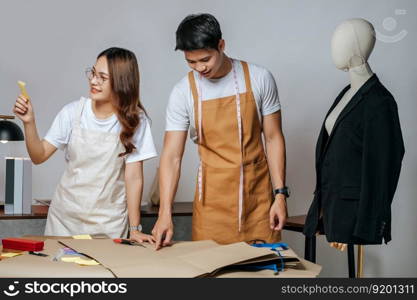 Portrait Young handsome man and pretty woman, Couple fashion designer working with scissor cutting on paper clothing pattern at the studio at home