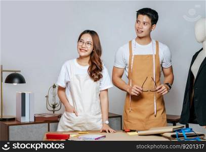 Portrait Young handsome man and pretty woman in glasses wearing apron, Couple fashion designer working together with happy, mannequin and tailoring tools on desk at studio