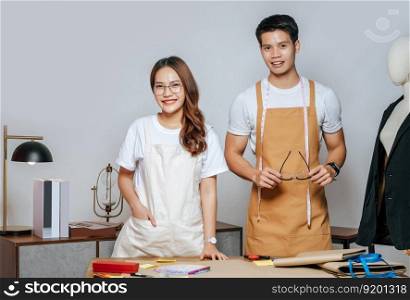 Portrait Young handsome man and pretty woman in glasses wearing apron, Couple fashion designer working together with happy, mannequin and tailoring tools on desk at studio