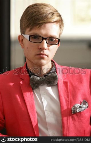 Portrait young handsome stylish man fashion model in glasses wearning bright red jacket and bow tie posing indoor
