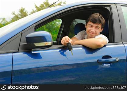 portrait young happy man showing the keys sitting in new car