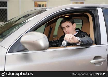 portrait young happy man showing the keys sitting in new car