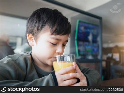 Portrait Young kid drinking fresh orange juice for breakfast in cafe, Happy child boy drinking glass of fruit juice while waiting for food in restaurant, Healthy food lifestyle concept