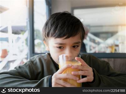 Portrait Young kid drinking fresh orange juice for breakfast in cafe, Happy child boy drinking glass of fruit juice while waiting for food in restaurant, Healthy food lifestyle concept