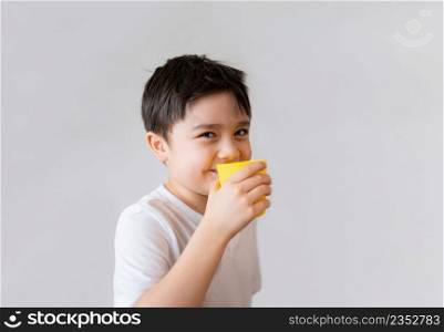 Portrait Young kid drinking fresh orange juice for breakfast, Isolated Happy child boy drinking glass of fruit juice and looking at camera with smiling face, Healthy kids food lifestyle concept