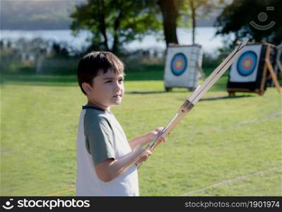 Portrait Young kid practising his archery, Mixed race child doing outdoors activity in summer camp adventure. School boy shooting bow with archery on training in sport school.