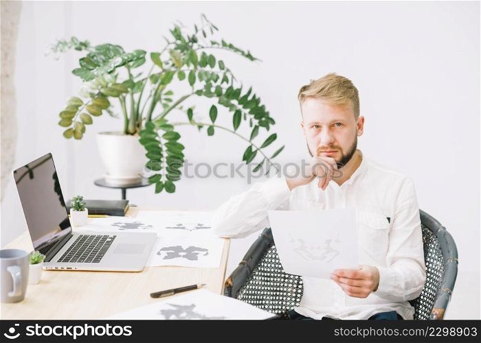 portrait young male psychologist holding rorschach inkblot test paper hand looking camera