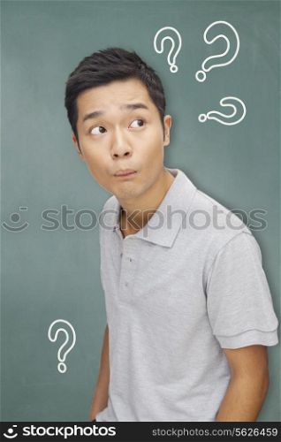 Portrait young man in front of blackboard with question marks