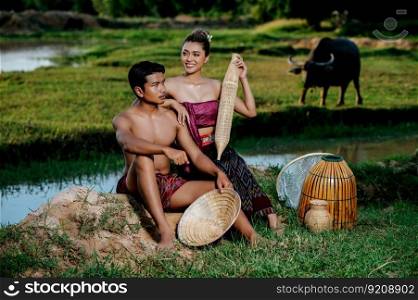 Portrait Young man topless sitting near pretty woman in beautiful clothes in rural lifestyle, bamboo fishing trap,  trap shrimp to catch fish or shrimp for cooking, blurred buffalo in background