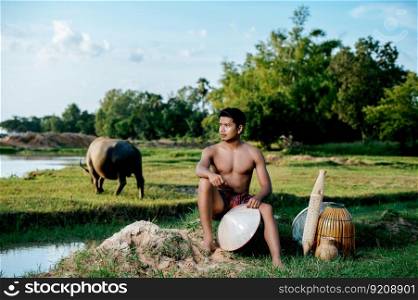 Portrait Young man topless wearing loinclothes in rural lifestyle sitting with bamboo fishing trap,  trap shrimp to catch fish or shrimp for cooking, blurred buffalo in background
