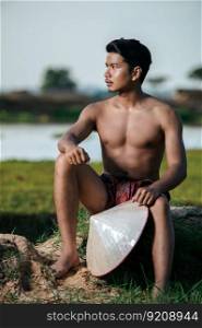 Portrait Young man topless wearing loinclothes in rural lifestyle sitting with bamboo fishing trap,  trap shrimp to catch fish or shrimp for cooking, blurred buffalo in background