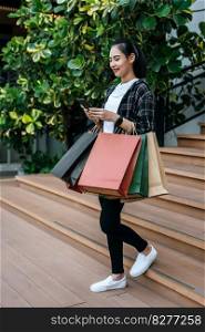 Portrait young woman carrying multiple shopping paper bag at shopping mall and use smartphone with smile while walking, New normal lifestyle with shopping concept
