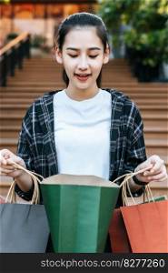 Portrait young woman carrying multiple shopping paper bag at shopping mall, she look inside with smile, New normal lifestyle with shopping concept