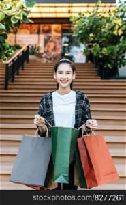 Portrait young woman carrying multiple shopping paper bag at shopping mall with smile, New normal lifestyle with shopping concept