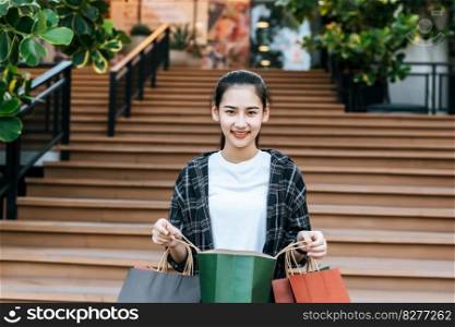Portrait young woman carrying multiple shopping paper bag at shopping mall with smile, New normal lifestyle with shopping concept