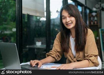 Portrait Young woman smile and looking to camera while working on laptop and paperwork or report presenting Project growth graph at cafe