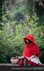 Portrait young woman with Little Red Riding Hood costume with apple and bread on basket in green tree park background