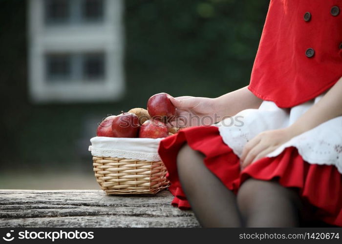 Portrait young woman with Little Red Riding Hood costume with apple and bread on basket in green tree park background